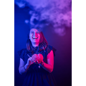 Une femme debout tient un cerveau en plastique au la main, et éclate de rire