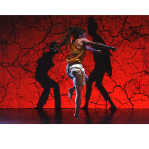 Un danseur debout su scène, deux ombres noires autour de lui, sur fond rouge